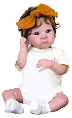 Image de Poupée de 45 cm, corps en plastique/coton, yeux bleus, cheveux implantés, cils collés. Combinaison courte à manches courtes de couleur beige, bandeau marron avec nœud, chaussettes blanches. Poupée réaliste.