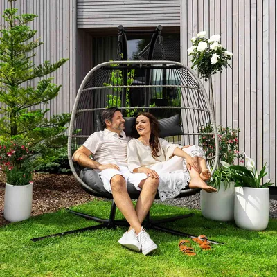 A couple relaxing in a hanging chair on a lawn in front of a modern house.
