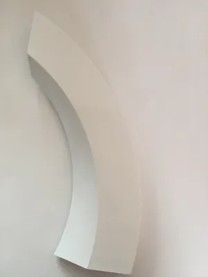 A white curved object is mounted on a white wall.