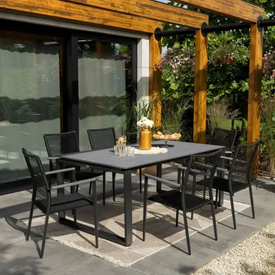 An outdoor dining set with a table and chairs under a wooden pergola with greenery in the background.