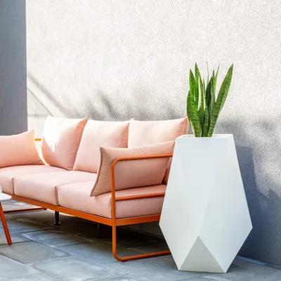 An outdoor patio scene with a pink sofa and a white geometric planter with a snake plant.