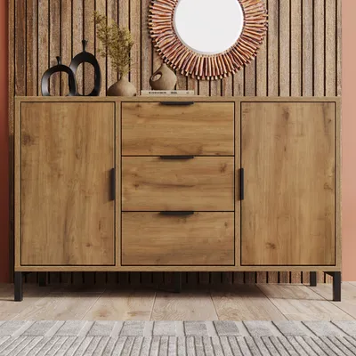 A wooden sideboard with three drawers and two doors, decorated with a mirror and vases on top, set against a wooden slatted wall.