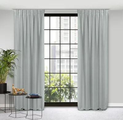 A room interior with a large window covered by light gray curtains. Two small side tables with decorative items are placed in front of the window.