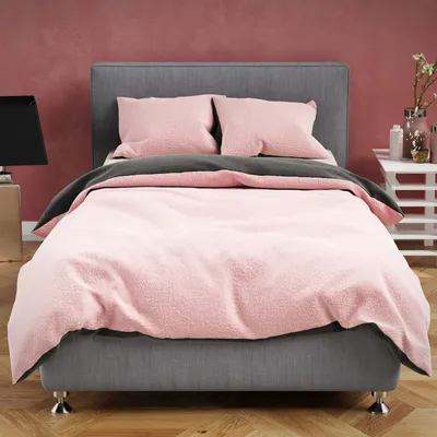 A bed with pink and anthracite bedding against a red wall.