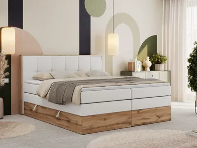 A bedroom scene featuring a large boxspring bed with a white upholstered headboard and a wood-effect base. The room has a modern, abstract mural on the wall and is decorated with plants and decorative items.