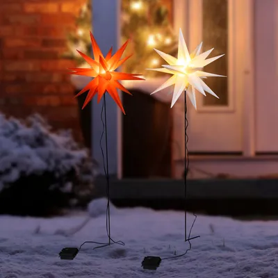 Two illuminated star-shaped lights in the snow outside a house at dusk.