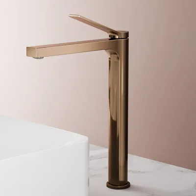 A rose gold faucet is shown in a studio setting, positioned next to a white sink on a marble countertop.
