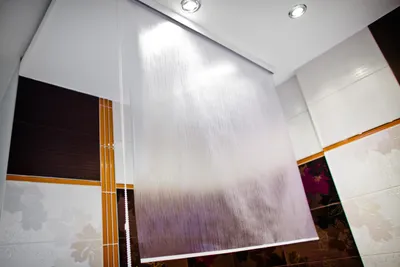 A roller blind is installed on the ceiling in a bathroom with tiled walls.