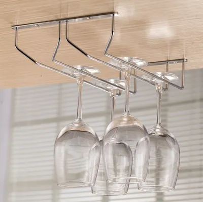 A metal wine glass rack mounted under a wooden surface, with four wine glasses hanging from it.