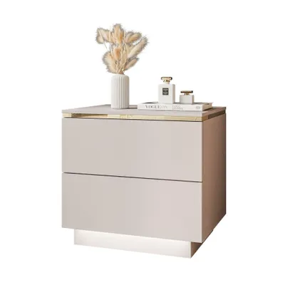 A modern beige nightstand with gold accents and LED lighting, decorated with a vase of dried flowers and perfume bottles.