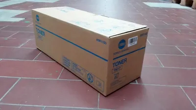 A cardboard box containing a toner cartridge sits on a tiled floor.