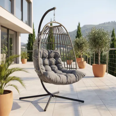 A hanging egg chair with cushions is placed on a tiled patio next to a modern building, with potted plants and a scenic mountainous background.