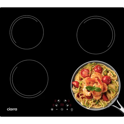 A black induction hob with four cooking zones and a pan of pasta with shrimp in the foreground.