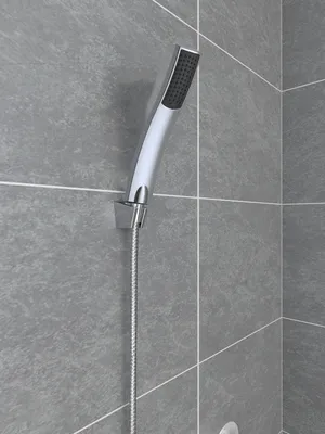 A close-up shot of a modern hand shower head mounted on a tiled wall.