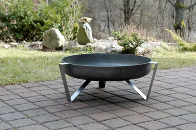 A metal fire pit sits on a paved patio in a garden setting.
