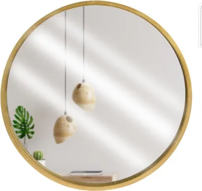 A round mirror with a golden wooden frame reflects a room with hanging pendant lights and a plant.