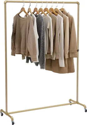 Several neutral-toned sweaters and a tan coat are displayed on a gold clothing rack.