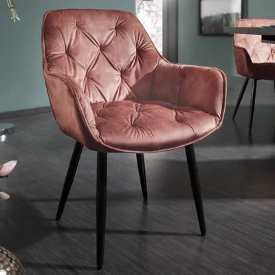 A close-up shot of a tufted velvet armchair with black metal legs, placed on a dark wooden floor.