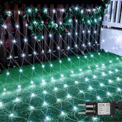 A net of white lights draped over a wooden fence and extending onto a green lawn, decorated with Christmas ornaments.
