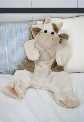 A plush cow toy is lying on a white bed with pillows.