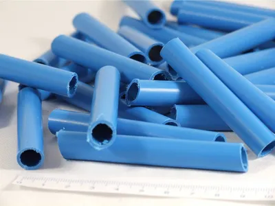 A pile of blue plastic tubes on a white surface with a ruler at the bottom.