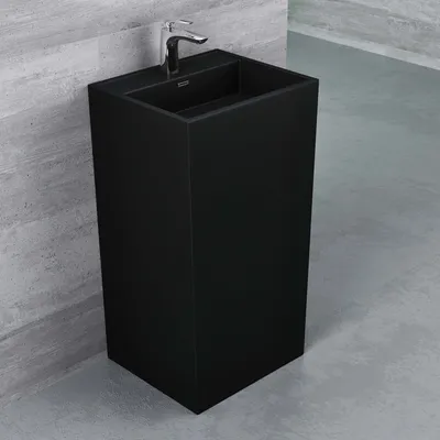 A black freestanding washbasin with a chrome faucet against a textured gray wall and a gray floor.