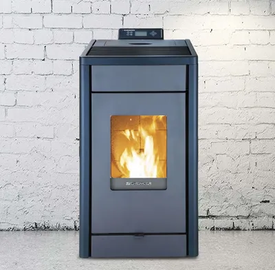 A black SCHENGER pellet stove with a visible flame is shown against a white brick wall and gray floor.