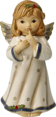 A ceramic angel figurine with wings, dressed in a white robe adorned with stars and blue trim. It has golden wings and a holly sprig on its head. The angel is holding a finger to its lips in a 'shushing' gesture.