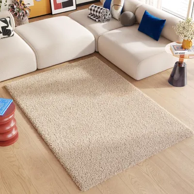 A beige shaggy rug is placed on a wooden floor in front of a modern, modular white sofa.