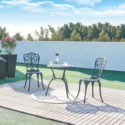 A bistro set with two chairs and a table on a wooden deck, with artificial grass and a white wall in the background.