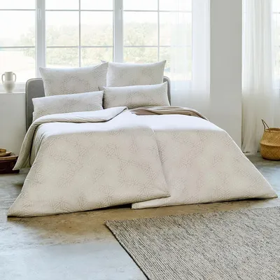 A neatly made bed with patterned bedding in a bright room with large windows.