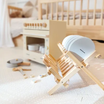 A wooden toy kitchen set with dishes drying on a rack.