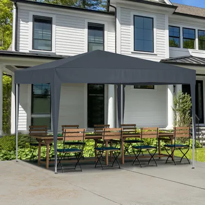 A gray pop-up canopy tent set up over a wooden table and chairs on a concrete patio in front of a white house.