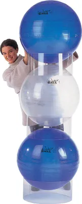 A woman is peeking from behind a stack of three exercise balls in a clear plastic holder.