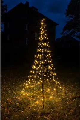 A decorative LED Christmas tree illuminated at night in a yard, with a dark house in the background.