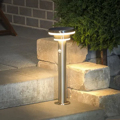 A solar-powered garden light is shown on outdoor steps next to a bush.