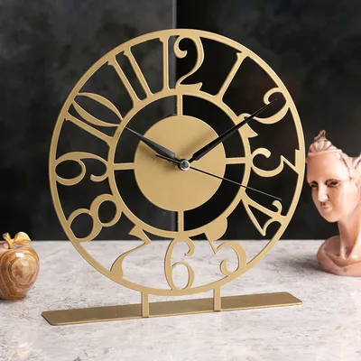 A decorative gold clock with Roman numerals is displayed on a marble surface, with a small decorative apple and a bust in the background.