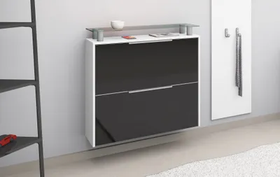 A modern, wall-mounted shoe cabinet with a glossy black front and a glass top shelf, shown against a light gray wall.