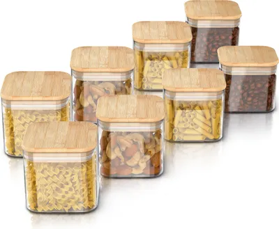 A set of glass storage jars with bamboo lids, filled with various dry goods like pasta and coffee beans, arranged on a white background.