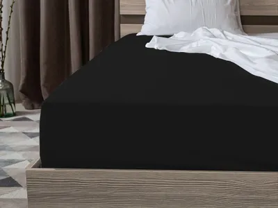 A black fitted sheet is shown on a bed with a white pillow and crumpled white sheet.