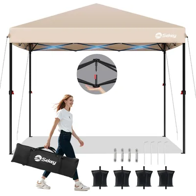 A woman is walking and carrying a folded canopy in a bag, with the canopy set up in the background. Accessories like sandbags and stakes are also displayed.