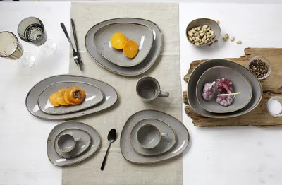 A collection of taupe-colored ceramic tableware, including plates, bowls, and cups, arranged on a light-colored textured surface.