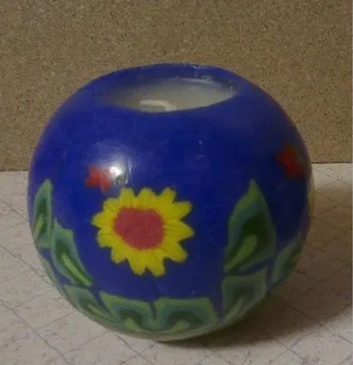 Eine Kugelkerze aus blauem Wachs mit einem Sonnenblumenmotiv und grünen Blättern.