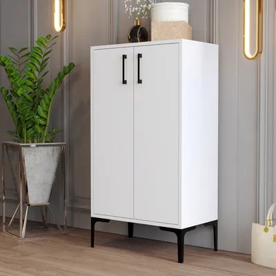 A white cabinet with black handles and legs, placed in a room with a plant and decorative items.