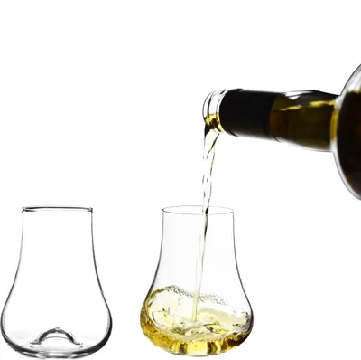 A bottle of white wine or spirit is being poured into a crystal glass, with another empty glass beside it.