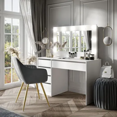 A modern white vanity table with illuminated mirror, a grey chair, and decorative elements in a well-lit room.