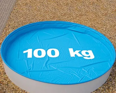 A blue pool cover with white text indicating weight capacity, placed on a gravel surface.