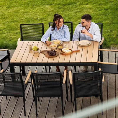 A couple is enjoying a meal at a wooden table on a deck, surrounded by a grassy lawn.