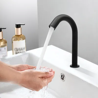Hands washing under a black automatic faucet in a modern bathroom sink.