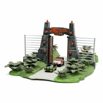 A miniature model of the Jurassic Park entrance gate with two toy vehicles and surrounding foliage.
